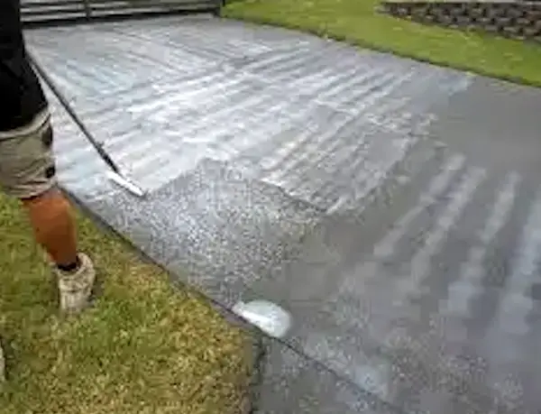 Hand applying second coat of concrete sealer with a roller, showing proper technique between coats