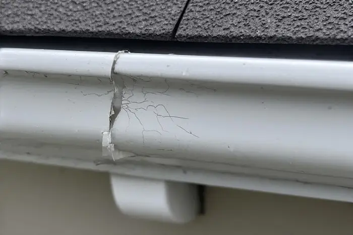 Close-up of failed gutter sealant showing cracking and poor adhesion on an aluminum gutter seam